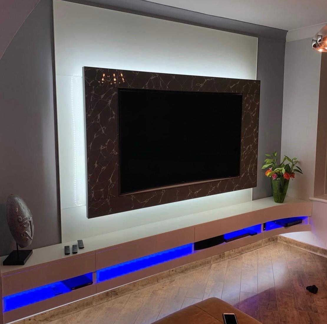 Bespoke TV wall with glass surround, illuminated white wall panel and blue-lit floating media storage.