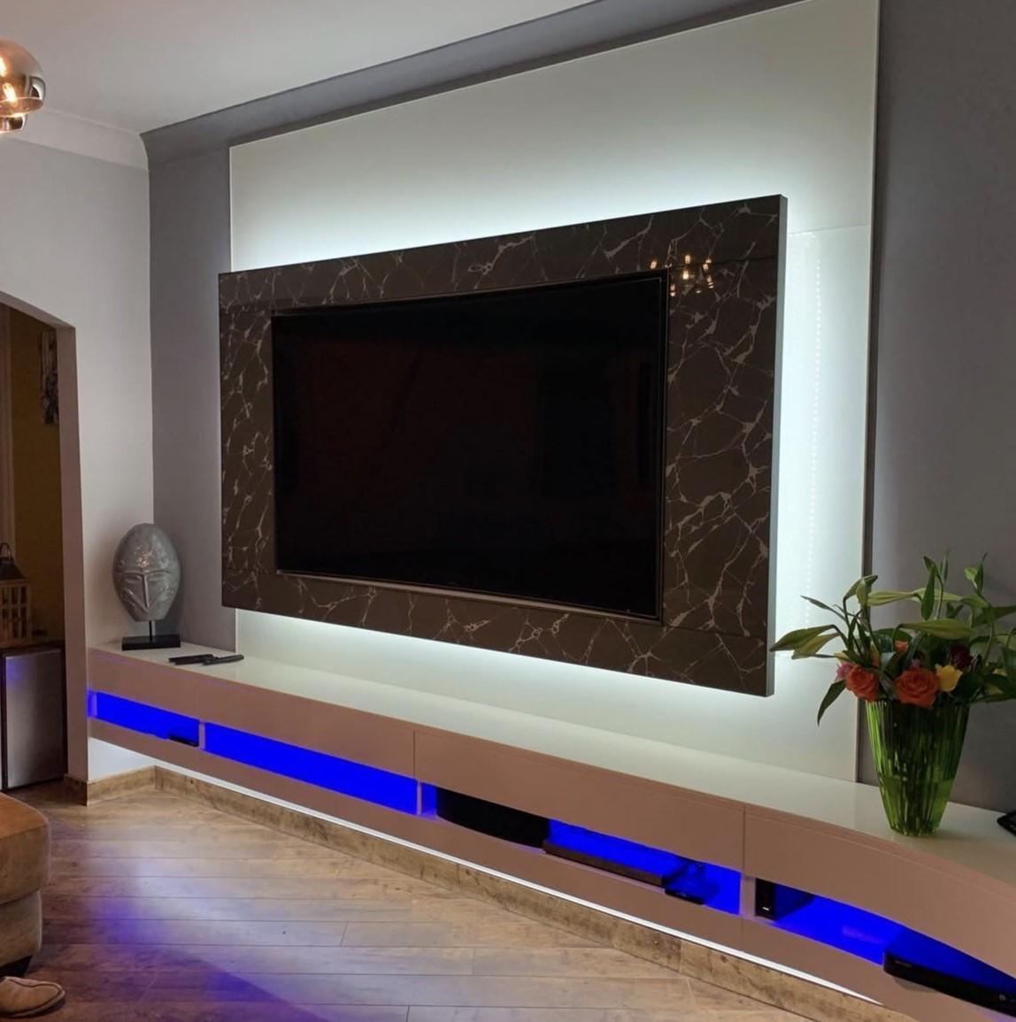 Bespoke glass TV wall with integrated white backlighting and a floating high-gloss media unit with blue LED lighting.
