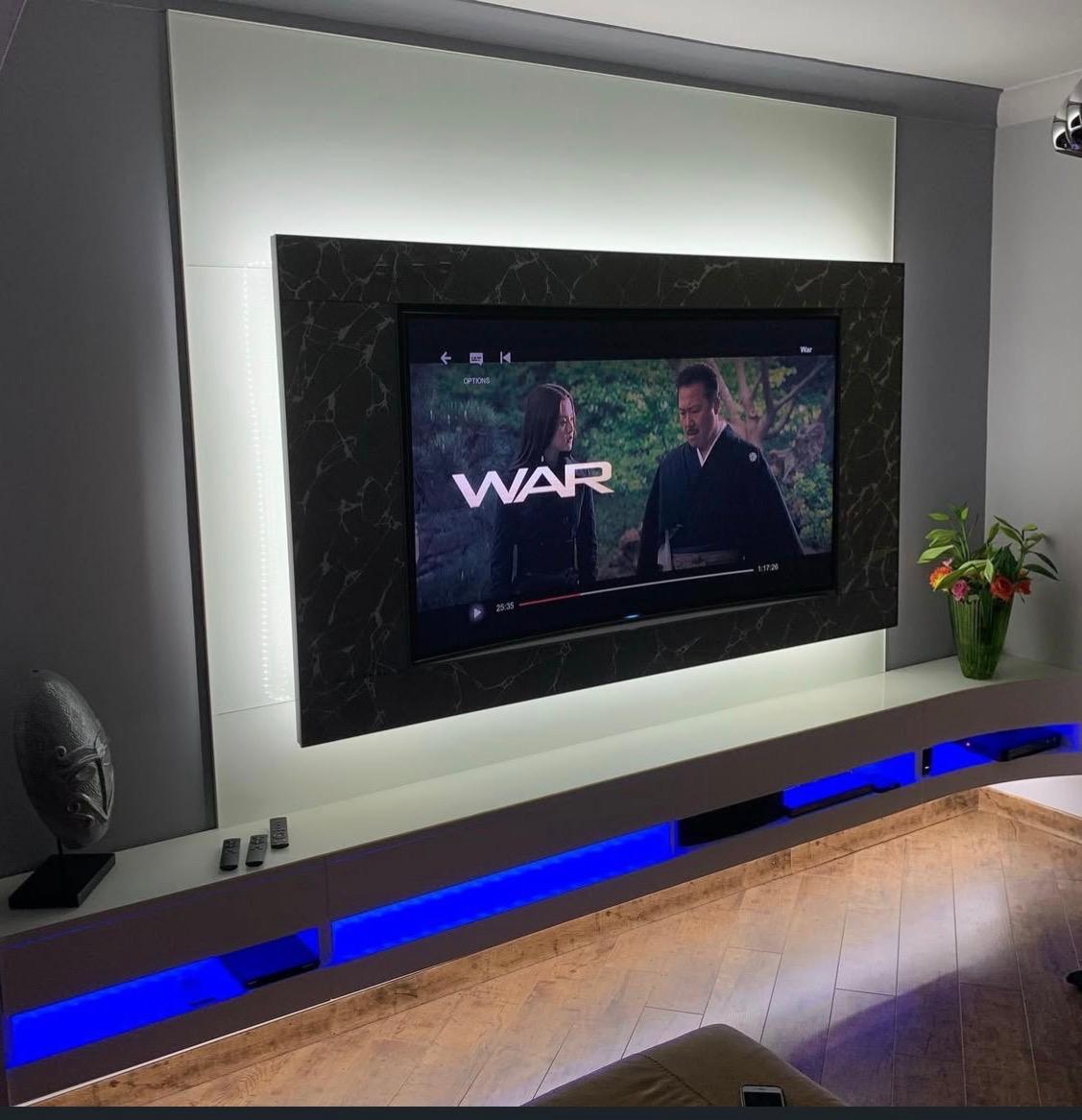 Illuminated bespoke TV wall and floating media unit shown with the television in use.
