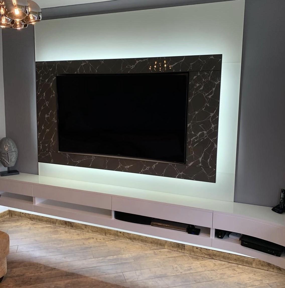 Front view of a bespoke glass TV wall with white integrated backlighting and a floating high-gloss media cabinet.