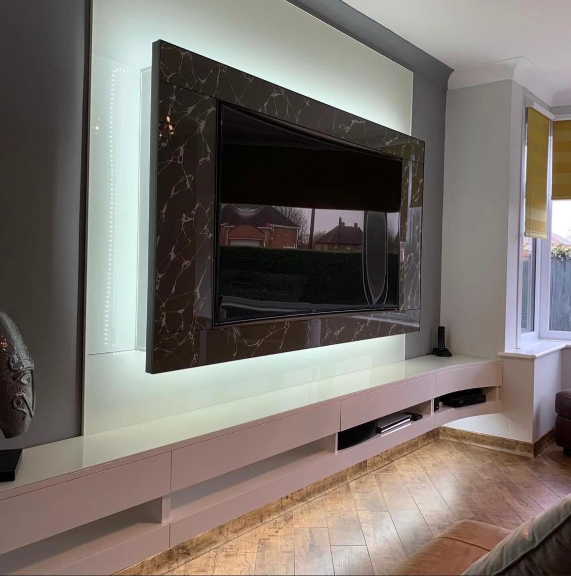 Angled view of a bespoke glass TV feature wall with integrated lighting and floating media storage.