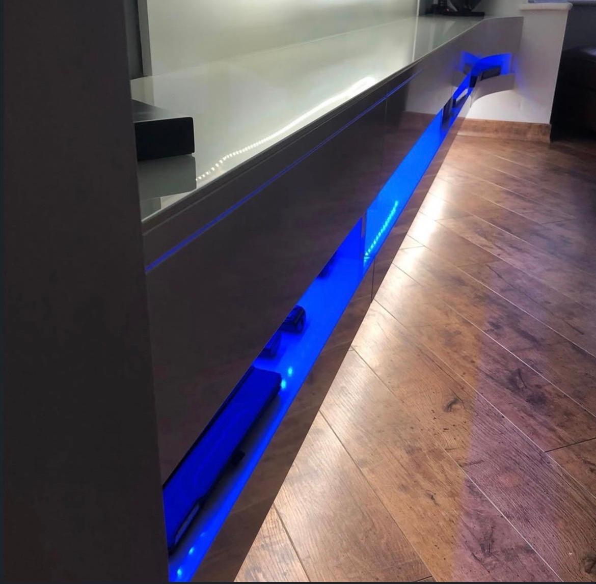 Close-up of the floating high-gloss media unit with blue LED-lit equipment bays and white accent lighting.