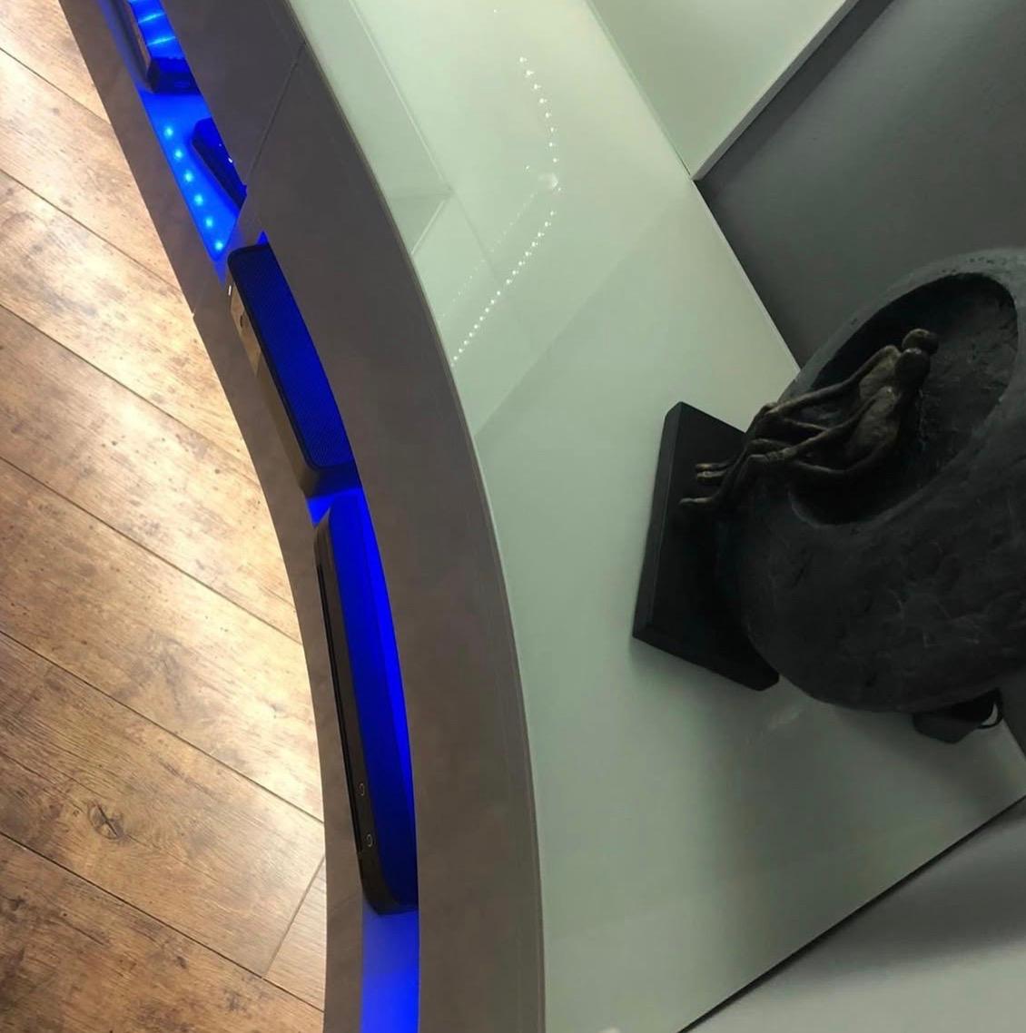 Detail of the floating high-gloss media unit with blue LED lighting beneath the glass feature wall.