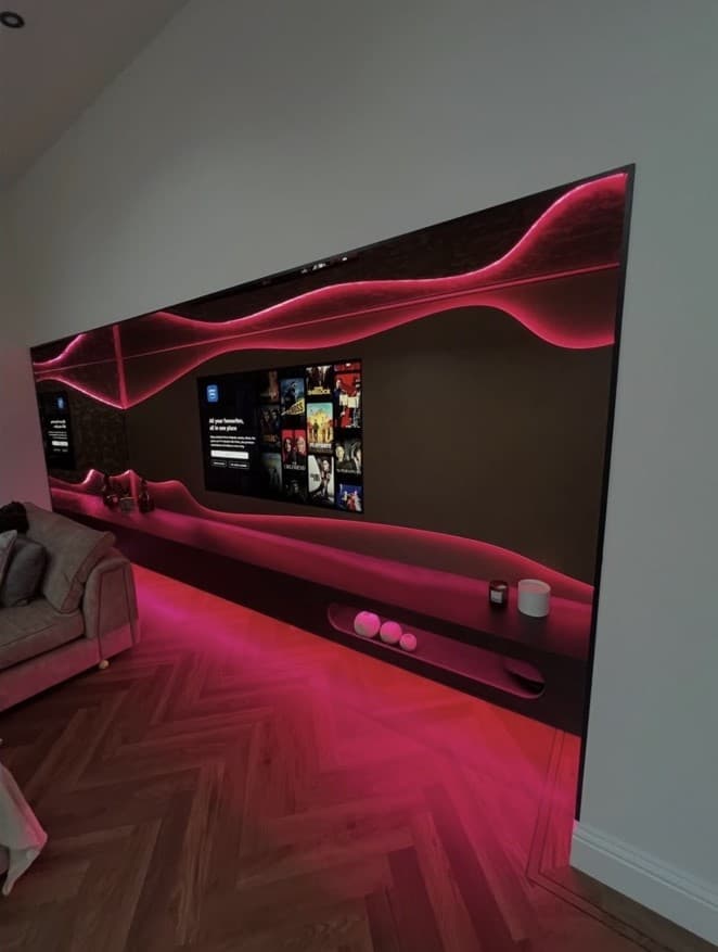 Cobra bronze and Cupra slate media wall illuminated in vivid pink with a long floating media unit.