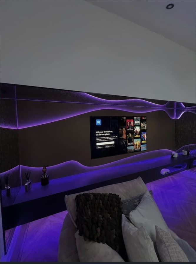 Media wall shown in use with purple integrated lighting and a long floating media shelf.