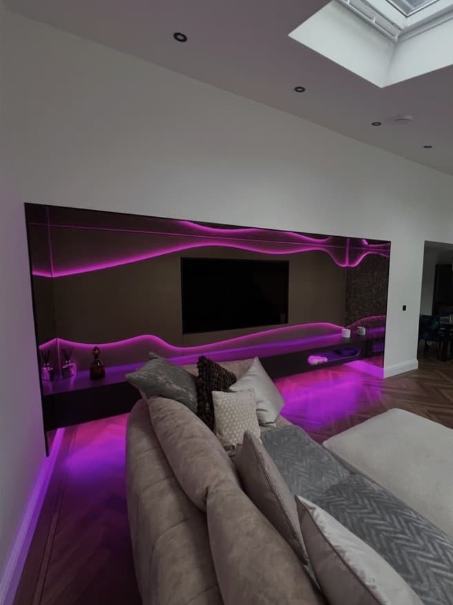 Wide living room view of the media wall illuminated in pink and purple with sculpted wave detailing.