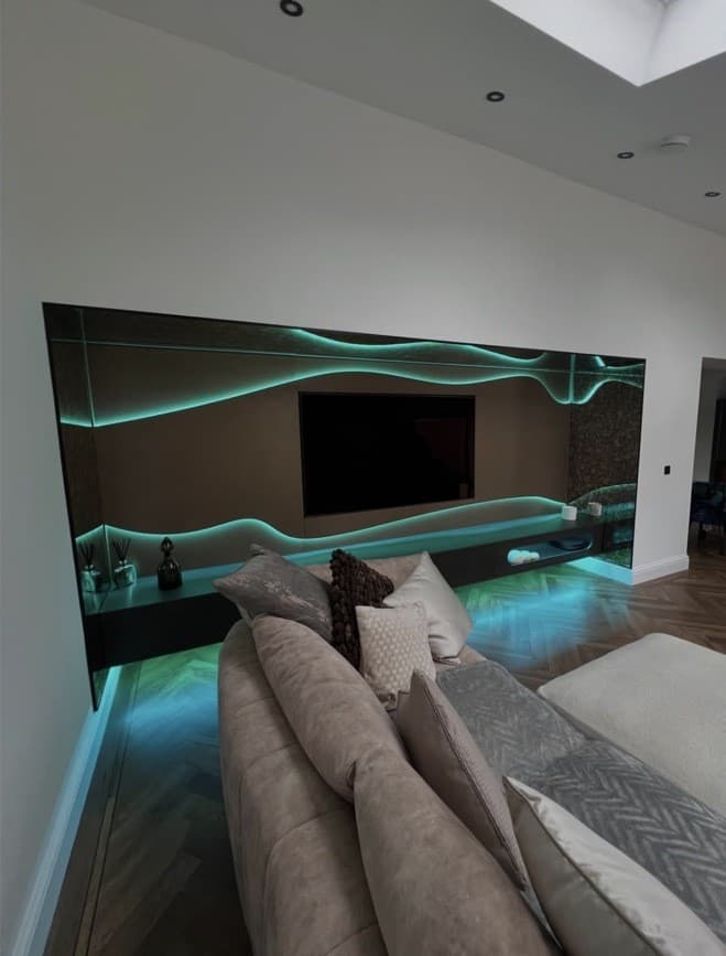 Living room view of the bespoke media wall with green illuminated wave detailing and floating cabinetry.