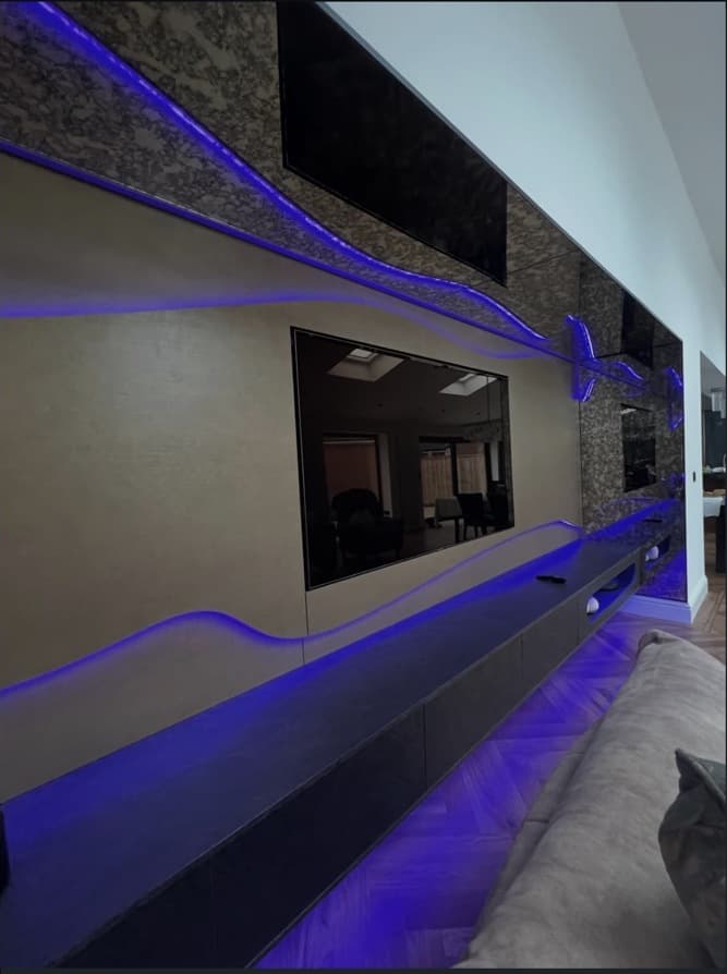 Long perspective view of the floating media cabinetry, textured wall panels and blue integrated lighting.