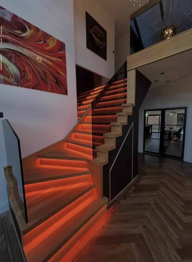 Bespoke oak staircase glowing with orange-red integrated step lighting and frameless glass balustrades.