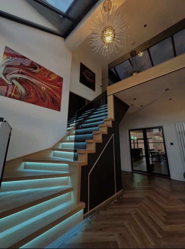 Oak staircase illuminated with cyan integrated step lighting and finished with frameless glass balustrades.