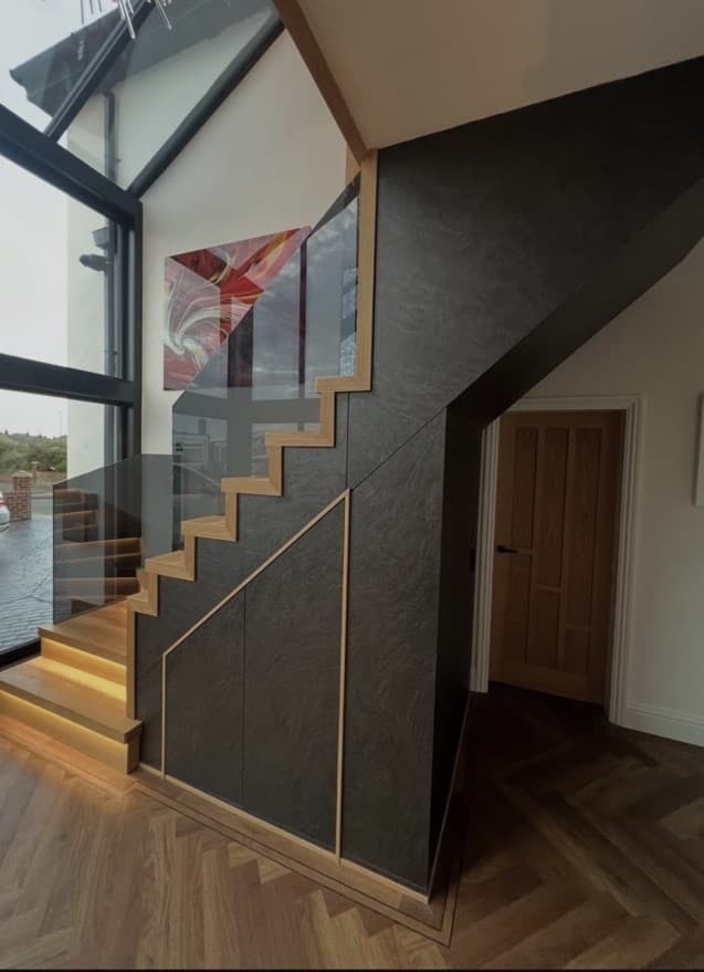 Side view of the oak staircase with frameless glass and precisely aligned dark under-stair feature panelling.