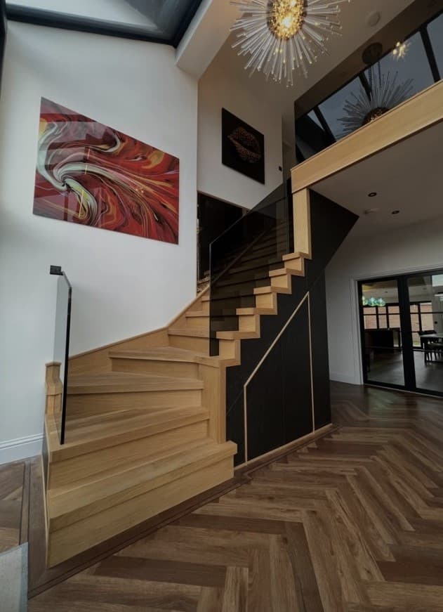 Daylight view of the bespoke oak staircase with frameless glass balustrades and precision-fitted dark under-stair panels.