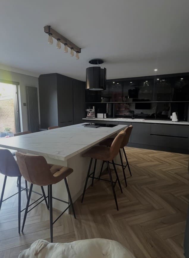 Wide view of a bespoke anthracite kitchen with Calacatta island, glass overhead cabinetry and herringbone flooring.