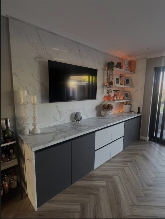 Angled view of the Calacatta marble media wall with floating storage and illuminated open shelving.