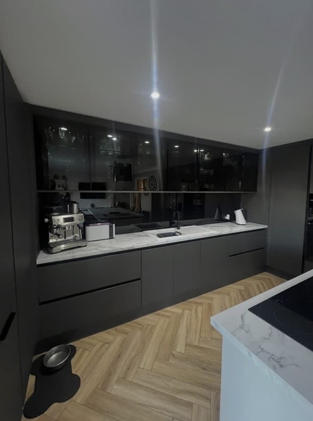 Close view of the anthracite kitchen cabinetry with dark glass splashback and glass overhead cupboards.