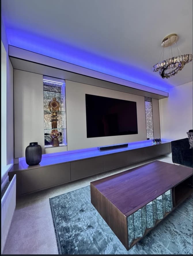 Angled view of the media wall with blue integrated lighting, floating cabinetry and illuminated mirrored display niches.
