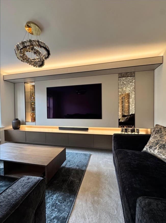 Bespoke brushed bronze and beige media wall with warm integrated lighting, floating cabinetry and mirrored display niches.