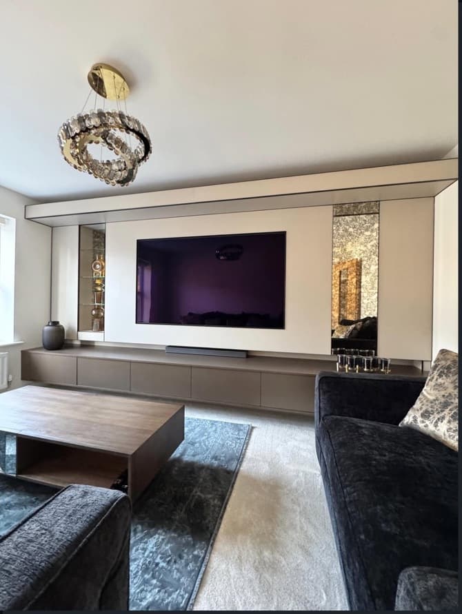 Straight-on view of a bespoke brushed bronze media wall with floating cabinetry, beige panels and mirrored display niches.
