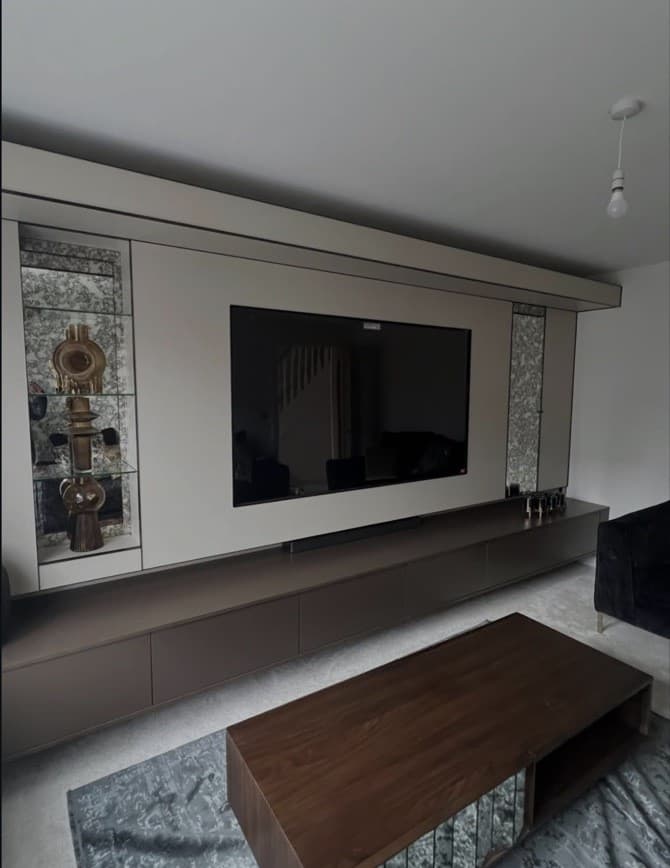 Side angle showing the bronze floating cabinetry, beige media panels and mirrored display niches.