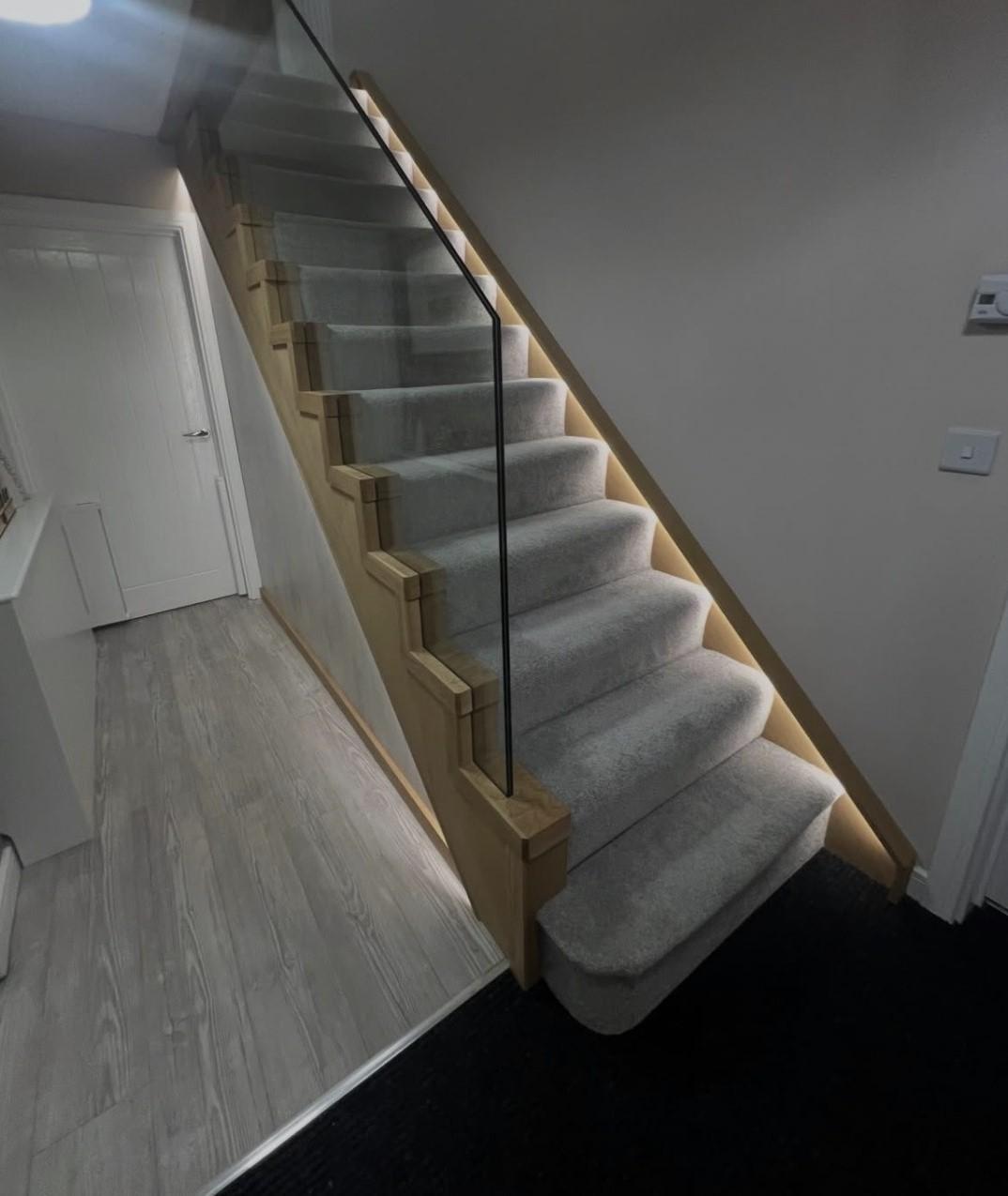 Bespoke oak and carpet staircase with frameless glass balustrade and warm integrated LED lighting along the stringers.