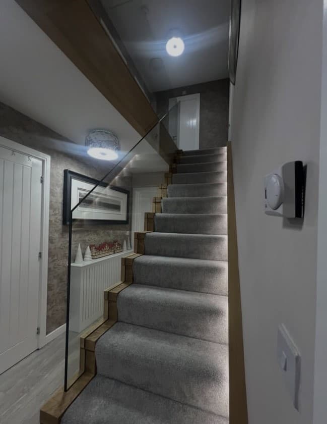 Straight view of the oak and carpet staircase with frameless glass and warm integrated lighting.
