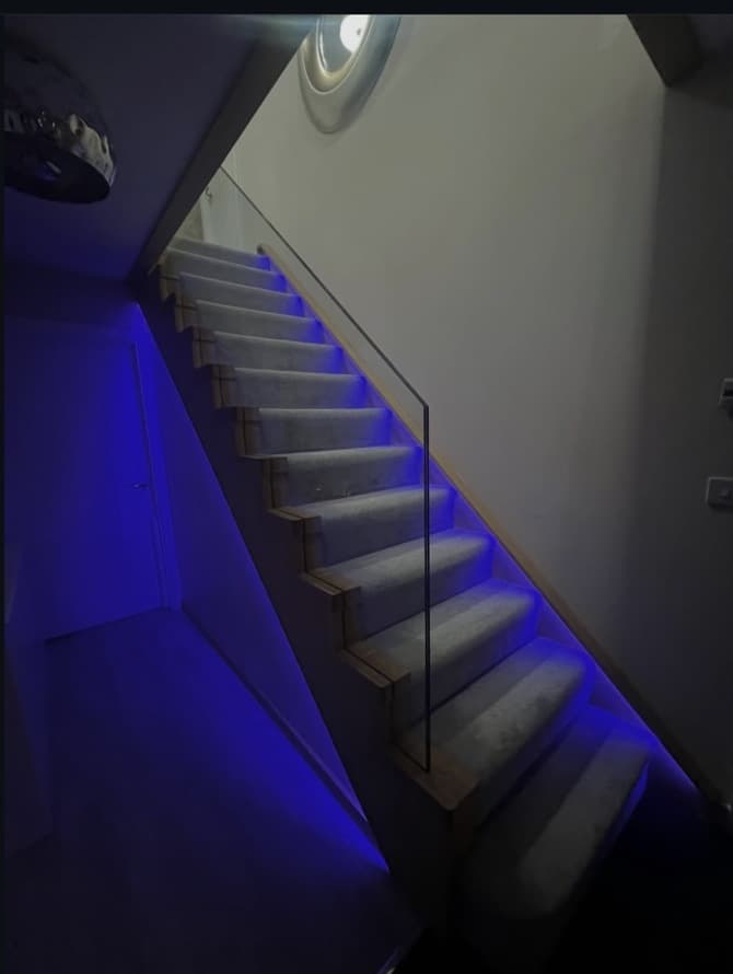 Oak staircase and frameless glass balustrade shown with blue colour-changing LED lighting fitted into the stringers.