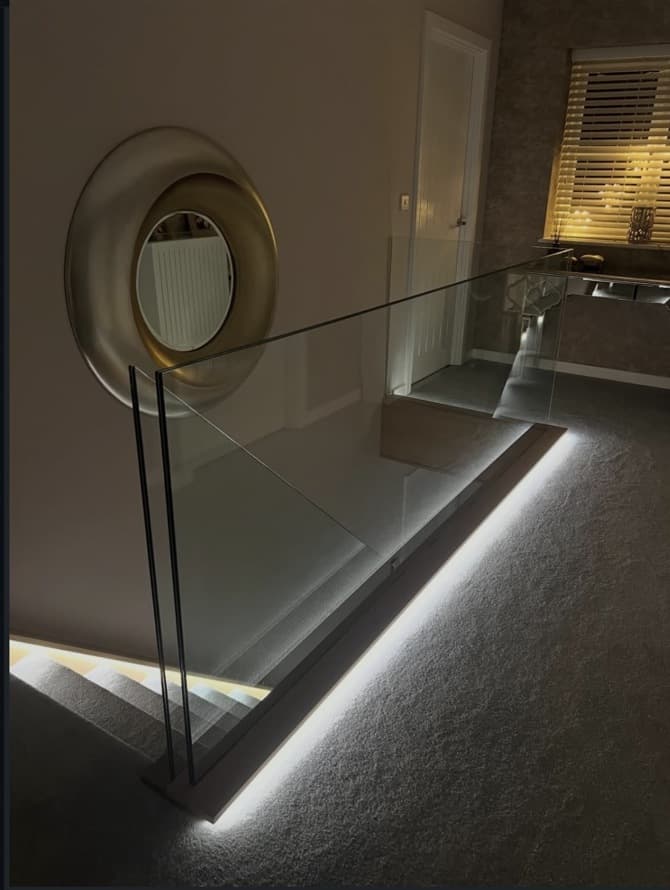 Frameless glass landing balustrade outlined by warm integrated lighting around the stair opening.