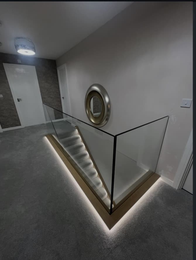 Upper landing with frameless glass balustrade, oak trim and warm LED lighting around the stairwell.