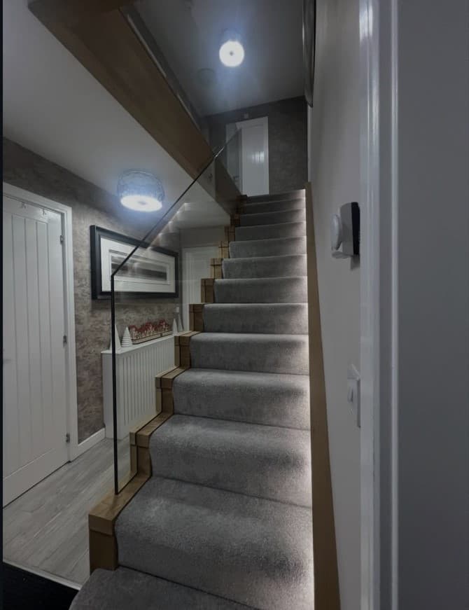 Front view up the carpeted oak staircase with frameless glass and integrated warm LED lighting.