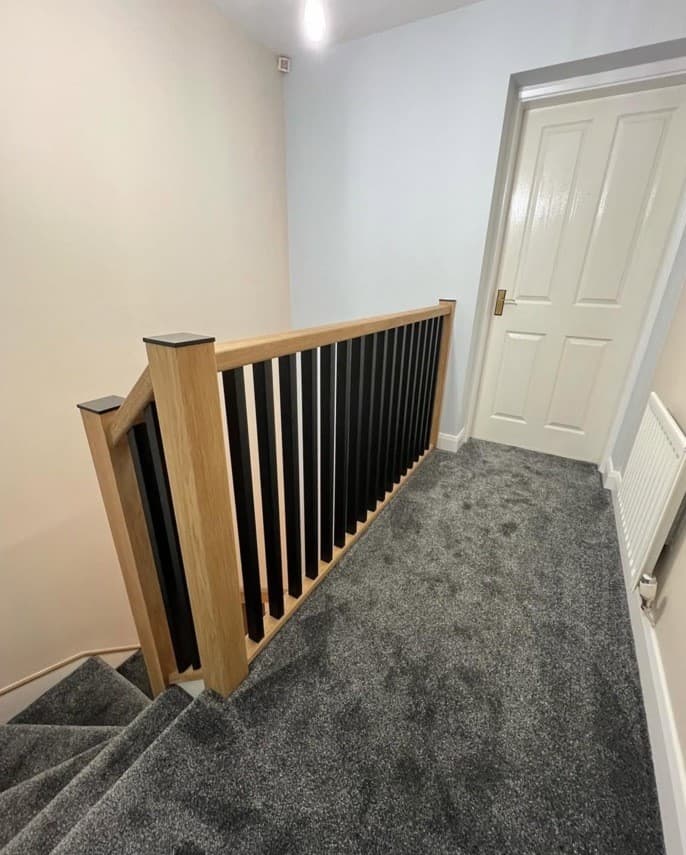 Finished upper landing with oak newel posts, black spindles and grey carpet.