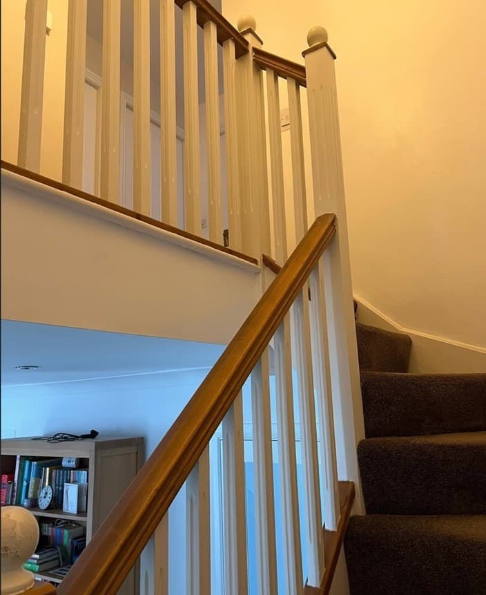 Upper staircase and landing before renovation with white spindles and traditional timber handrail.