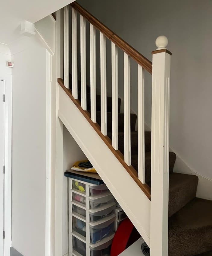 Staircase before renovation with white spindles and open under-stair storage.