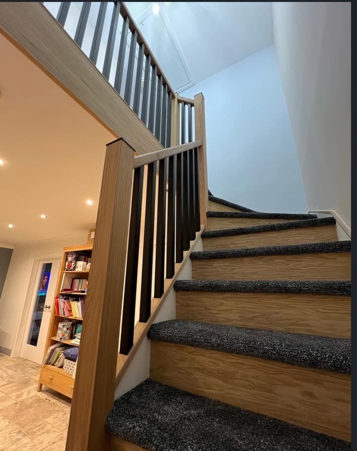 Close view up the renovated oak staircase with black spindles and dark carpet.