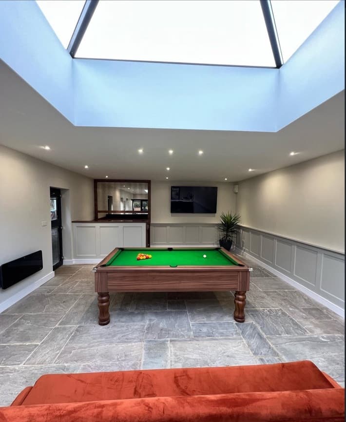 Grey panelled wall in the games room with television and stone flooring.