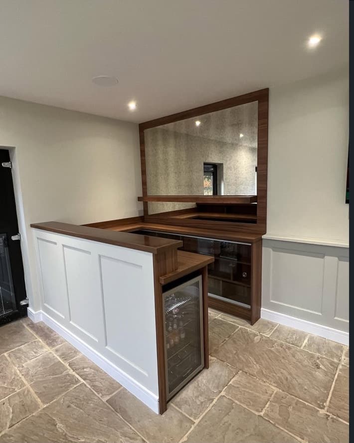Bespoke timber home bar with integrated drinks fridge, storage, wall panelling and a large antique mirror.
