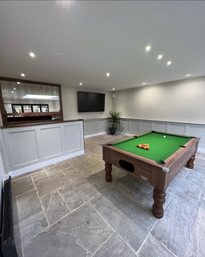 Wide games-room view with pool table, grey wall panelling and the bespoke bar visible beyond.