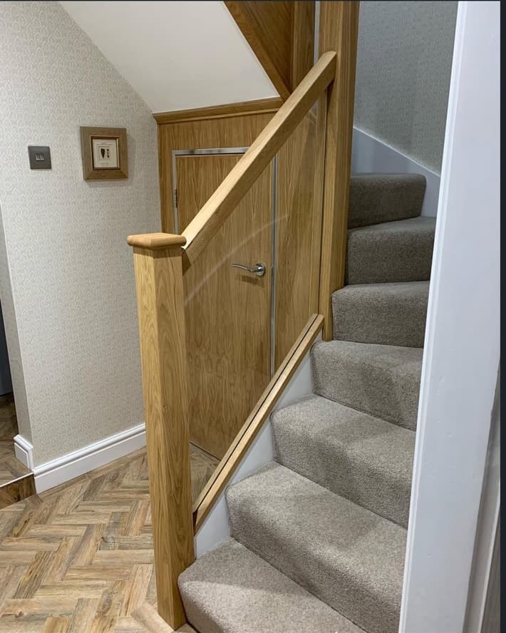 Finished oak and glass staircase renovation with carpeted steps and integrated oak under-stair door.