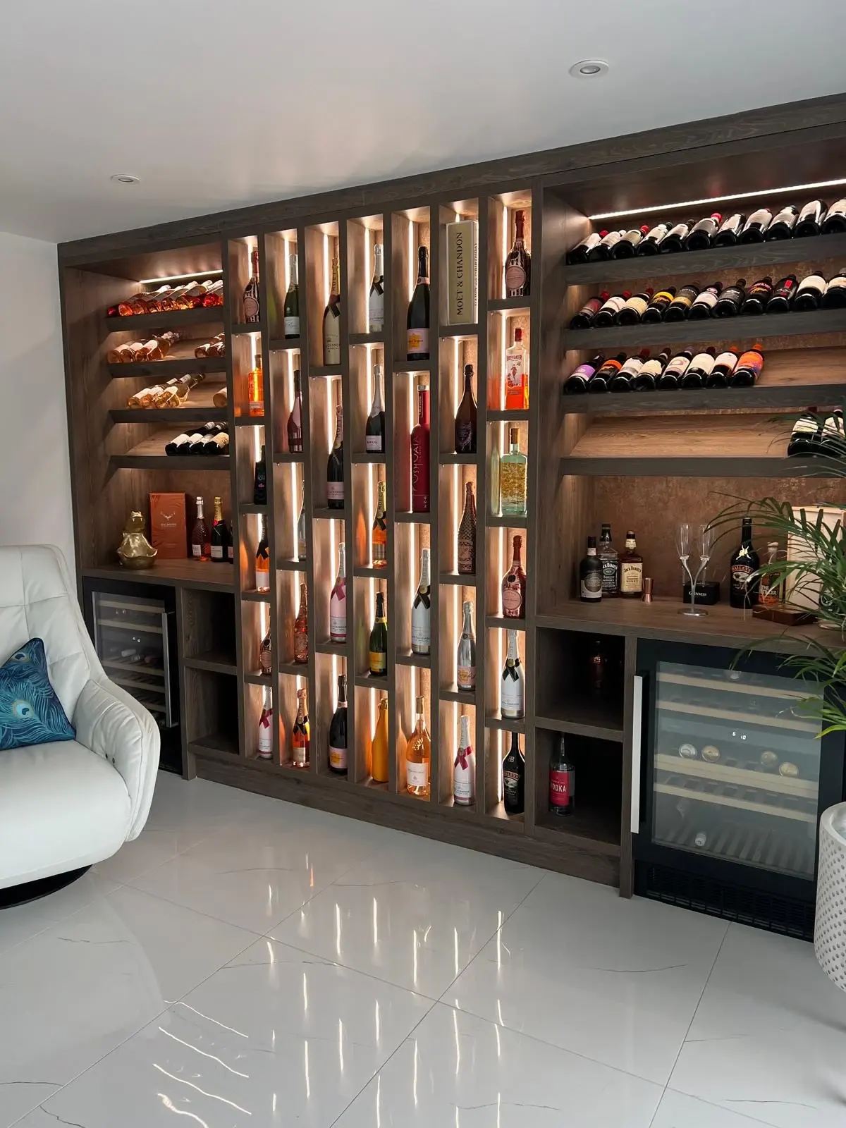 Angled close view of illuminated bottle compartments, horizontal wine racks and a wine cooler.