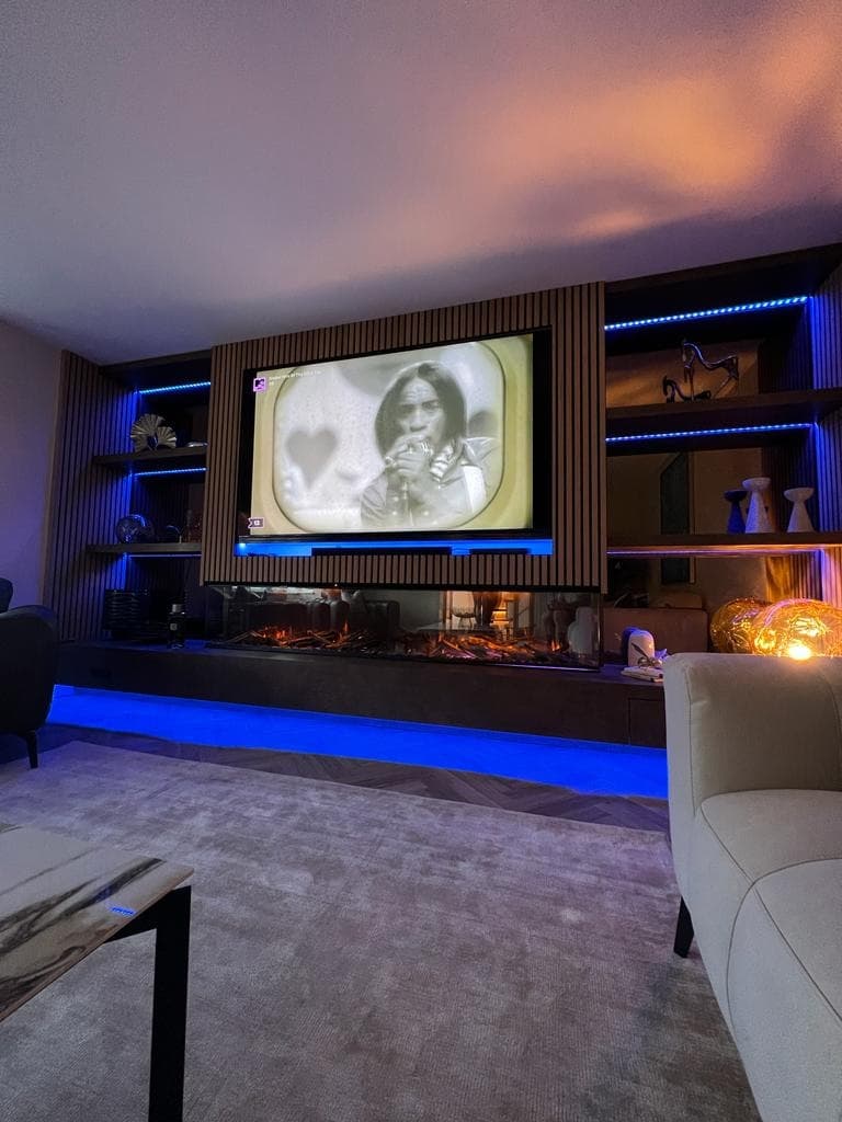 Left-side view of the illuminated media wall with TV, shelving and fireplace.