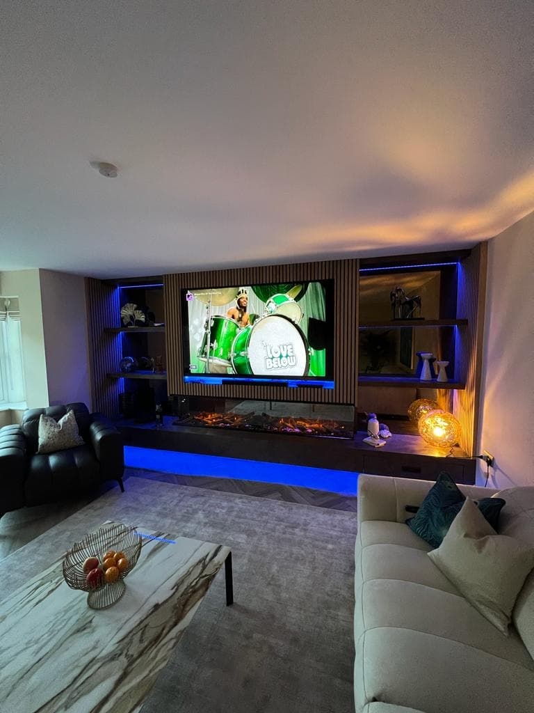 Angled room view showing the media wall, illuminated shelves, oak acoustic panels and long fireplace.
