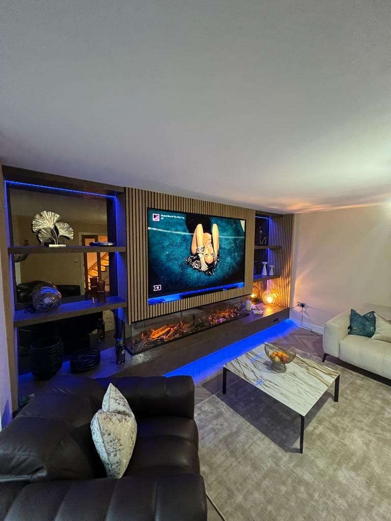 Wide living-room view of the oak slatted media wall with illuminated shelving and integrated fireplace.