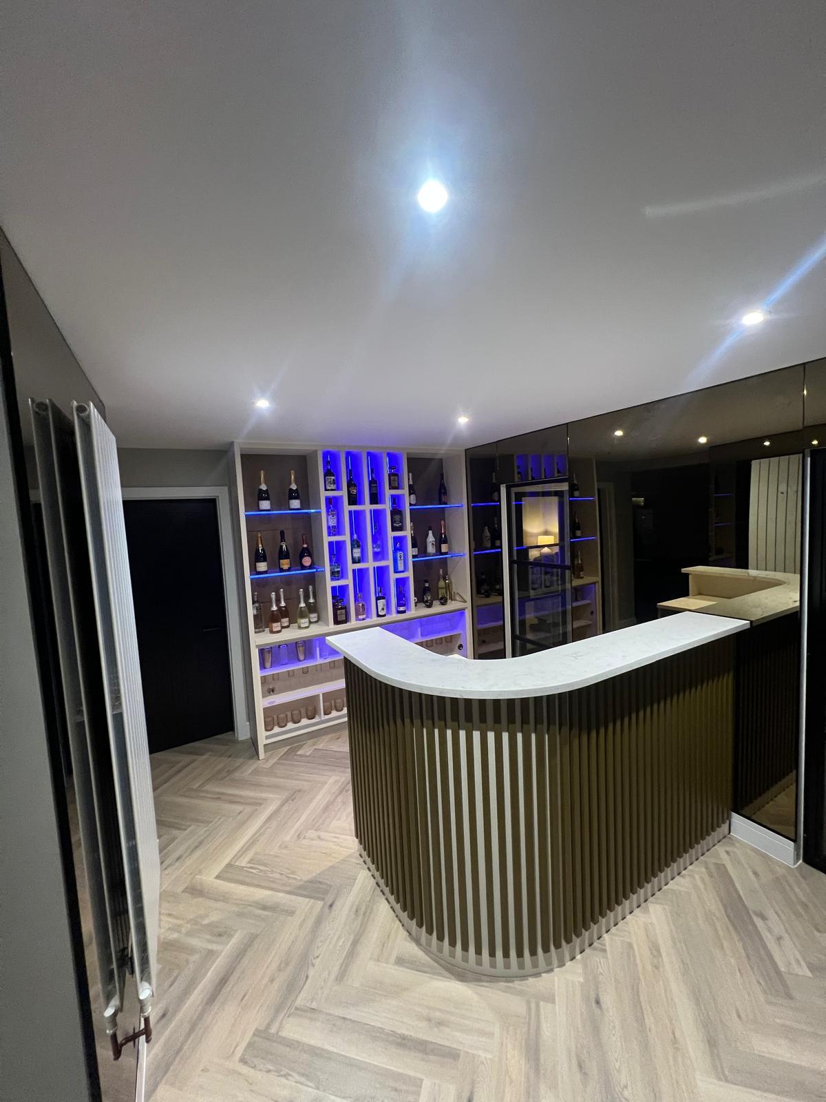 Bespoke home bar with a curved reeded front, white worktop and bottle display.