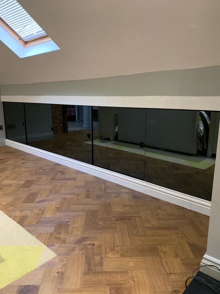 Grey mirrored glass wardrobes fitted beneath a sloping loft ceiling.
