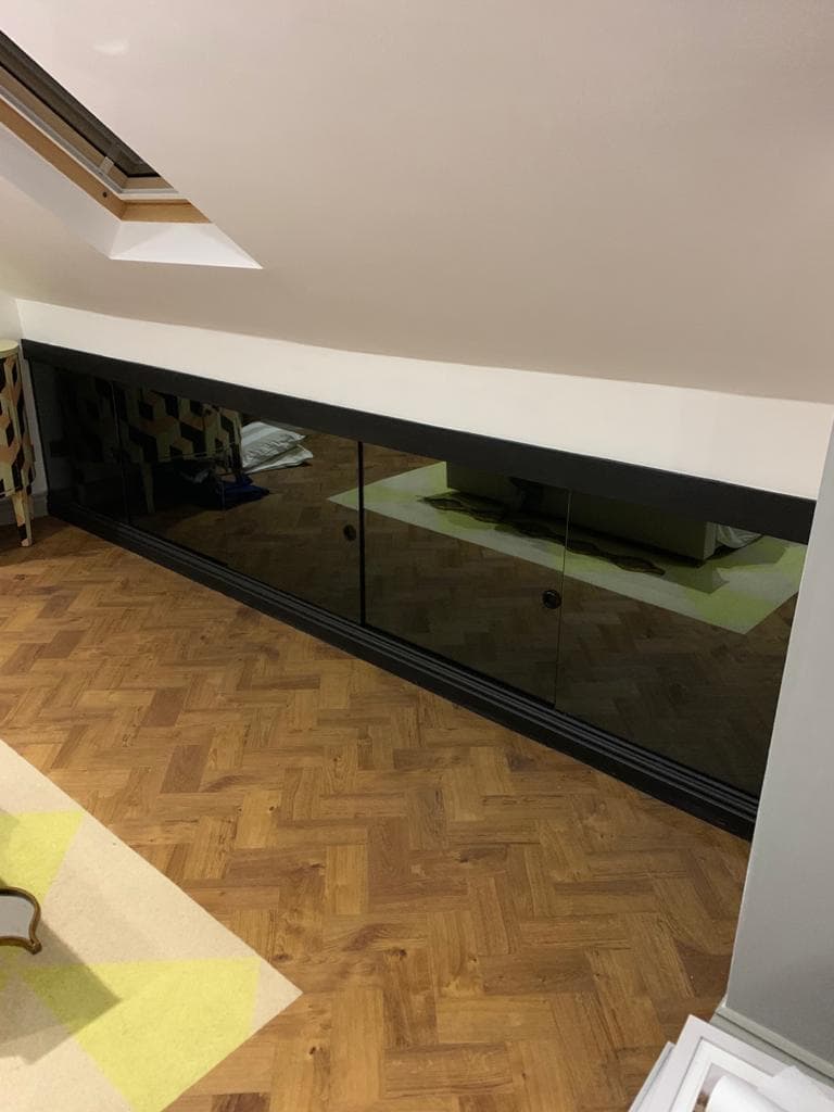 Grey mirrored glass wardrobes fitted beneath a sloping loft ceiling.