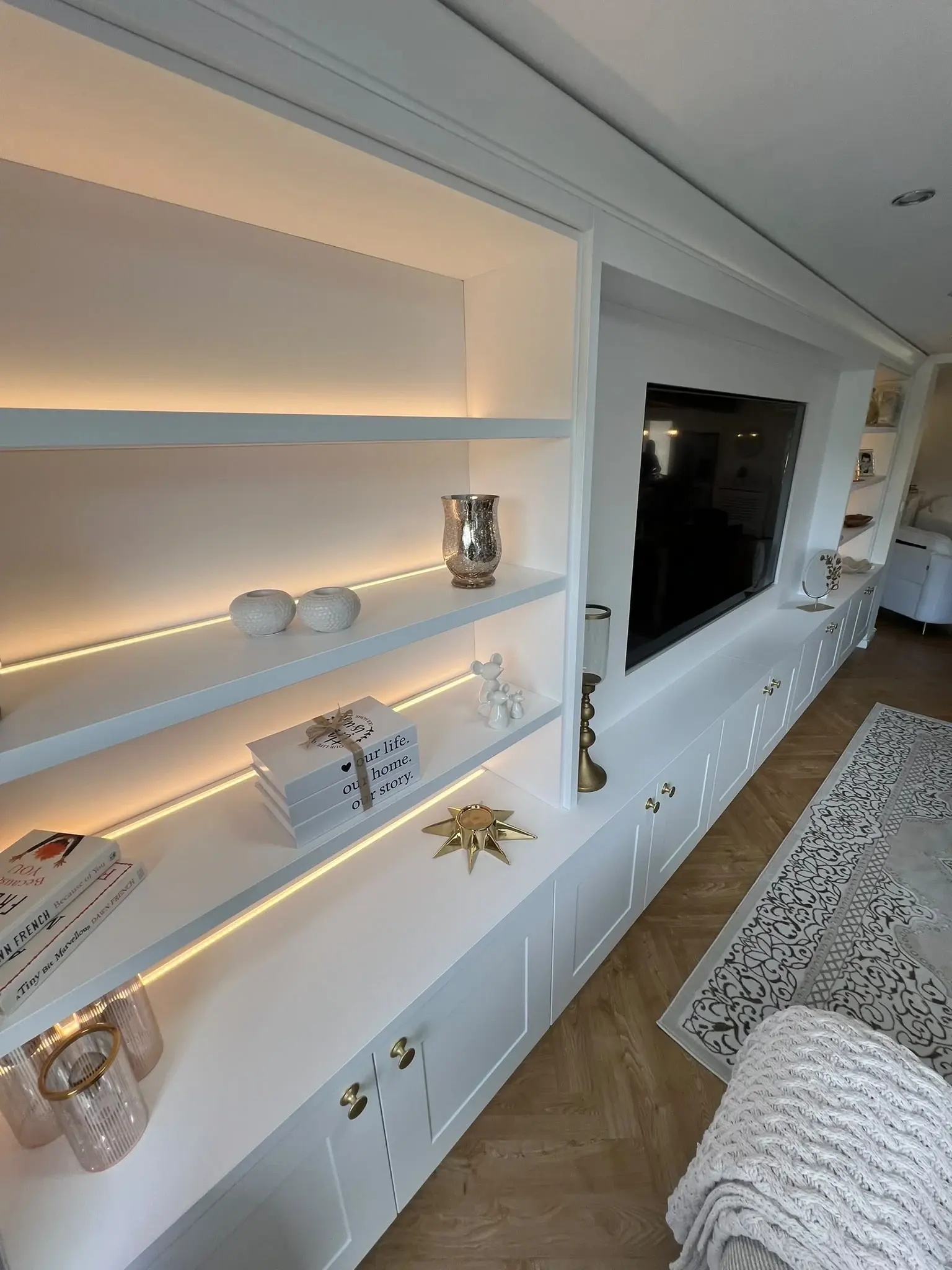 Angled detail of the media wall with illuminated shelves and shaker-style lower cupboards.