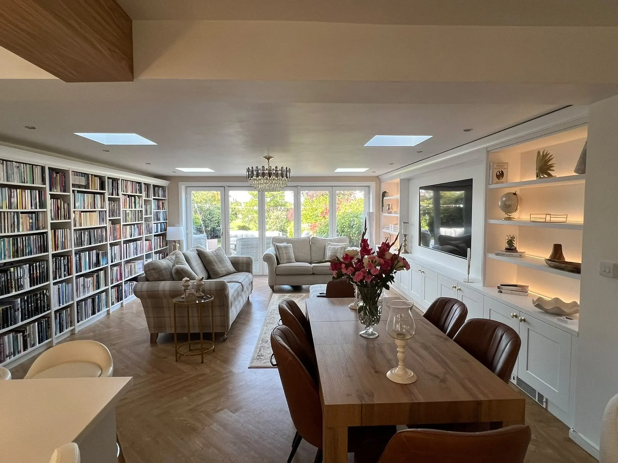 View across the dining table towards the living area, bookcase wall and fitted media wall.