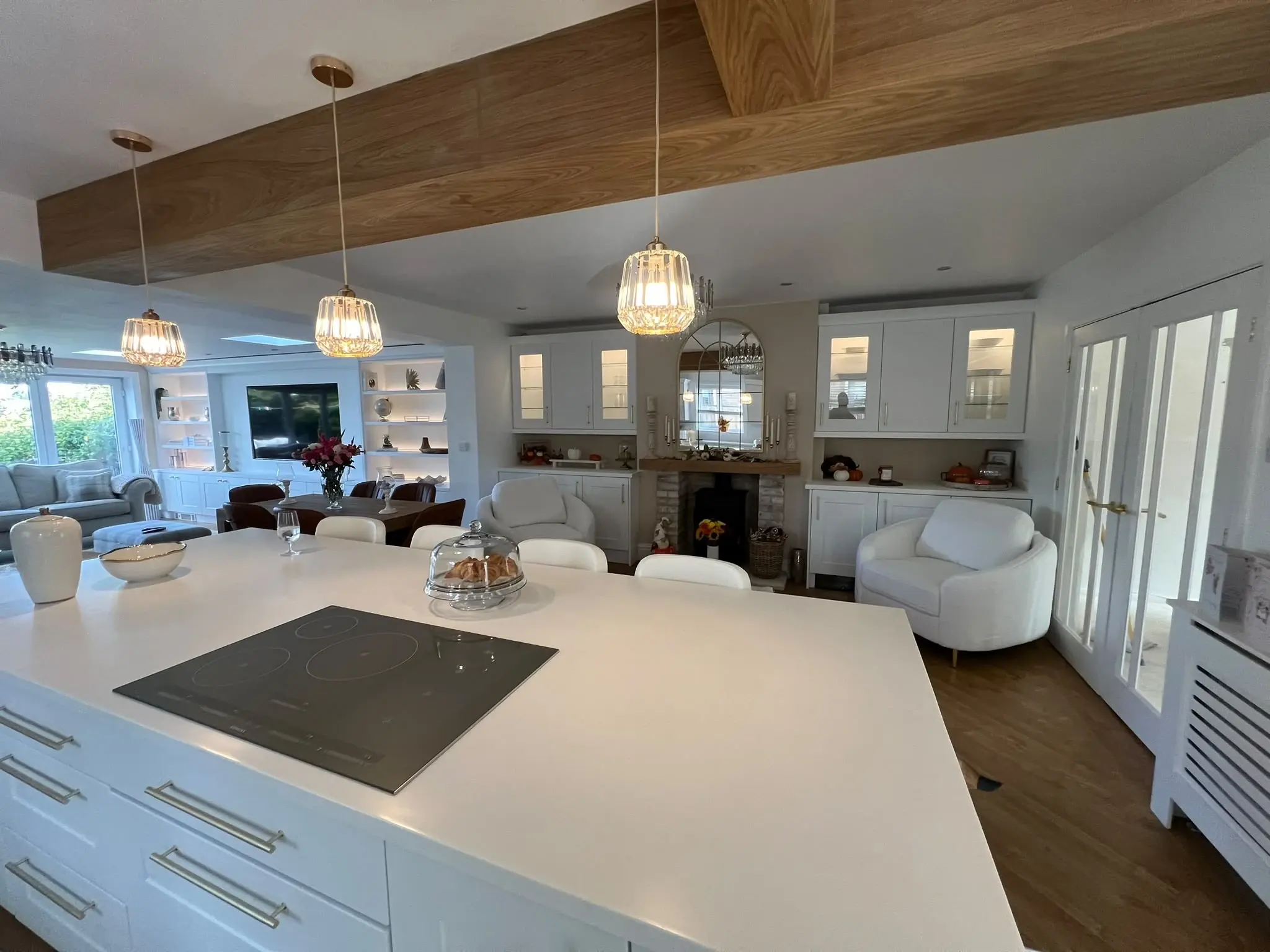 White kitchen island with an inset hob, looking towards matching fireplace cabinetry and the living area.