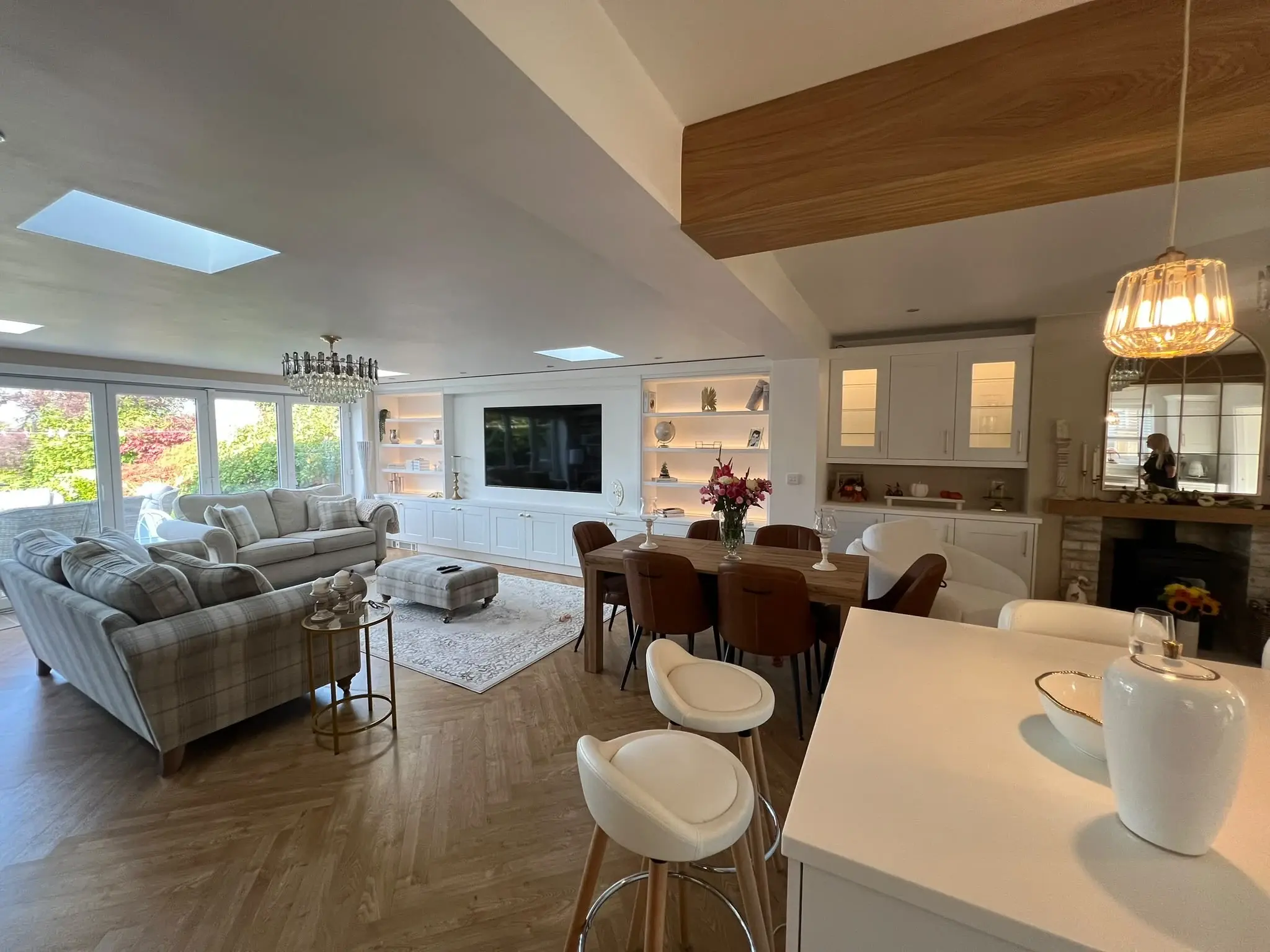 Wide kitchen-to-living-room view with the white island, dining area and fitted media wall.