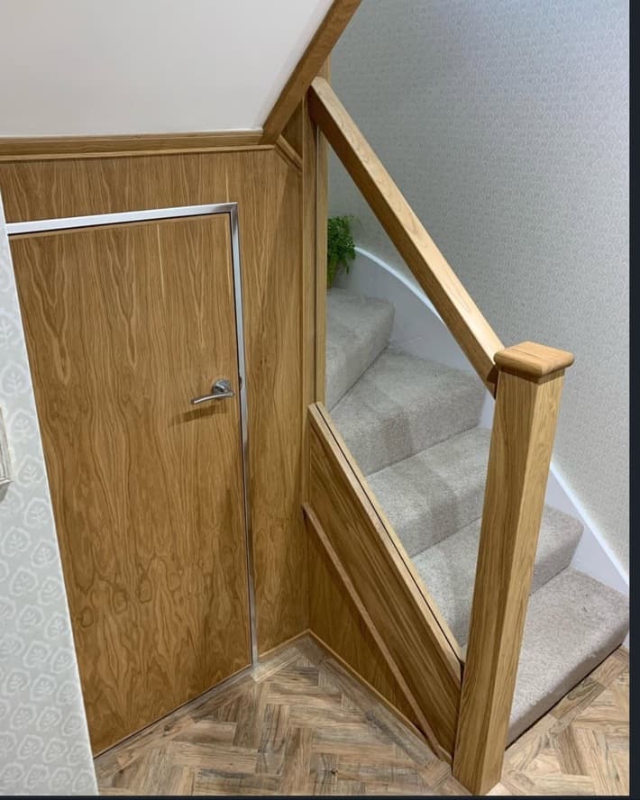 Lower staircase detail showing oak posts, clear glass balustrade and integrated oak under-stair joinery.