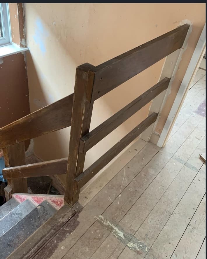 Staircase before renovation with an old dark timber balustrade and unfinished surrounding walls.